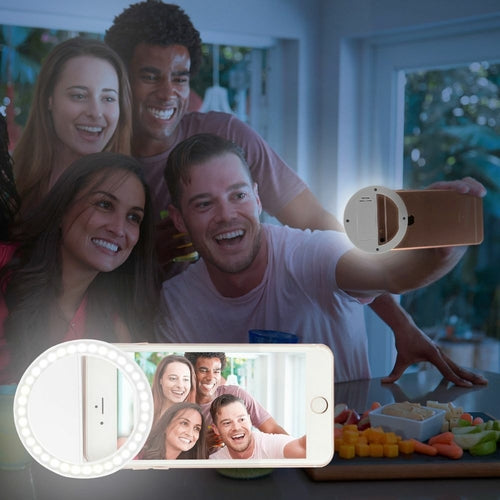 People taking a selfie with a smartphone using a ring light, with a blurred background of a dining area.